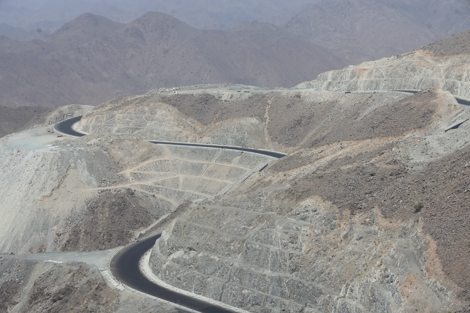 Mountain road switchbacks climbing Jabal Al Deem through benched rock cuttings